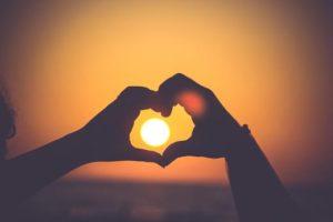 Hands held in heart shape with sun in the background