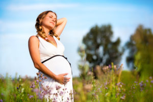 Pregnant woman standing in field with trees and blue sky in background